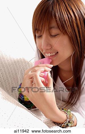 Stock Image - Young woman listening to personal stereo. Fotosearch