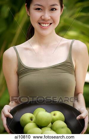 Young woman looking at camera, holding a bowl of apples View Large Photo Image Stock Image - Young woman looking at camera, holding a bowl of apples. Fotosearch