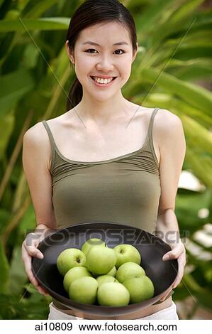 Young woman looking at camera, holding a bowl of apples View Large Photo Image Stock Photo - Young woman looking at camera, holding a bowl of apples. Fotosearch