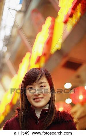 Stock Photo - Young woman looking at camera, neon signs behind her. Fotosearch
