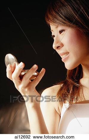 Young woman looking at compact mirror, smiling View Large Photo Image Stock Image - Young woman looking at compact mirror, smiling. Fotosearch