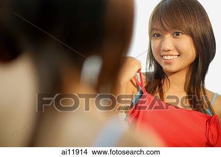 Young woman looking at mirror, holding up tank top View Large Photo Image Picture - Young woman looking at mirror, holding up tank top. Fotosearch