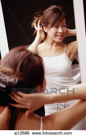 Young woman looking at mirror touching her hair View Large Photo Image Stock Photograph - Young woman looking at mirror touching her hair. Fotosearch