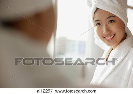 Young woman looking at mirror, towel wrapped around her head View Large Photo Image Stock Photo - Young woman looking at mirror, towel wrapped around her head. Fotosearch