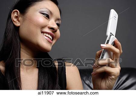 Young woman looking at mobile phone, smiling View Large Photo Image Stock Photo - Young woman looking at mobile phone, smiling. Fotosearch