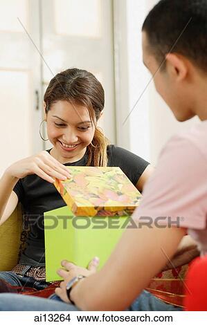 Young woman looking into gift box, young man sitting in front of her View Large Photo Image Picture - Young woman looking into gift box, young man sitting in front of her. Fotosearch