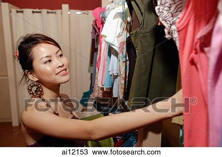 Stock Image - Young woman looking through clothes rack. Fotosearch