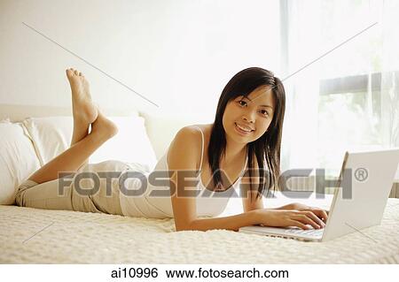 Young woman lying down on her bed, using laptop, looking at camera View Large Photo Image Stock Photograph - Young woman lying down on her bed, using laptop, looking at camera. Fotosearch