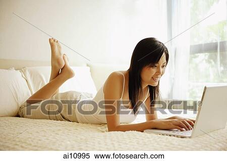 Young woman lying down on her bed, using laptop View Large Photo Image Stock Photography - Young woman lying down on her bed, using laptop. Fotosearch
