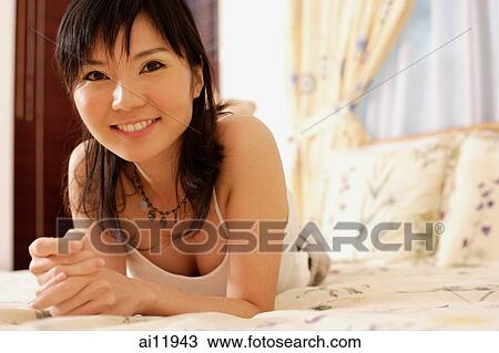 Stock Image -  Young woman lying on bed, hands clasped. Fotosearch