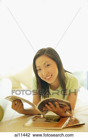 Young woman lying on bed, holding magazine, looking at camera View Large Photo Image Stock Image - Young woman lying on bed, holding magazine, looking at camera. Fotosearch