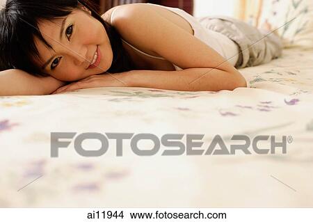 Picture -  Young woman lying on bed, looking at camera. Fotosearch