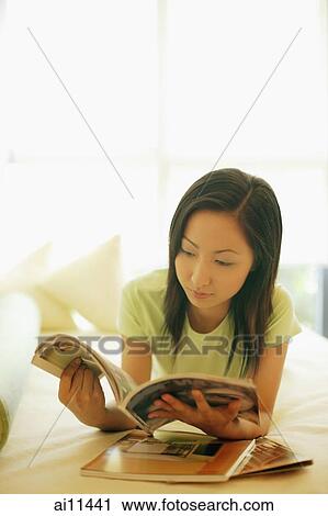Young woman lying on bed, reading magazine View Large Photo Image Stock Image - Young woman lying on bed, reading magazine. Fotosearch