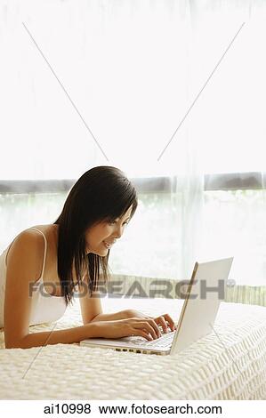 Young woman lying on bed, using laptop View Large Photo Image Stock Photo - Young woman lying on bed, using laptop. Fotosearch
