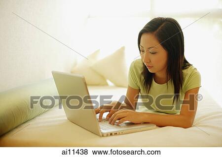 Young woman lying on bed, using laptop View Large Photo Image Stock Photo - Young woman lying on bed, using laptop. Fotosearch