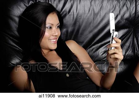 Young woman lying on chair, holding mobile phone View Large Photo Image Stock Photo - Young woman lying on chair, holding mobile phone. Fotosearch