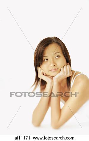 Stock Image - Young woman lying on floor, hands on chin, looking away. Fotosearch
