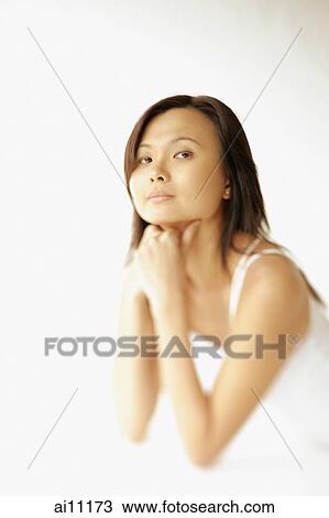 Stock Image - Young woman lying on floor, hands on chin, looking at camera. Fotosearch