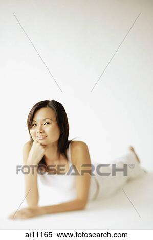 Young woman lying on floor, hands on chin, looking at camera View Large Photo Image Stock Photography - Young woman lying on floor, hands on chin, looking at camera. Fotosearch