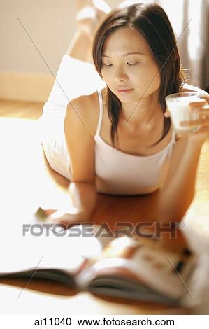 Young woman lying on floor holding a glass, flipping through magazine View Large Photo Image Stock Image - Young woman lying on floor holding a glass, flipping through magazine. Fotosearch