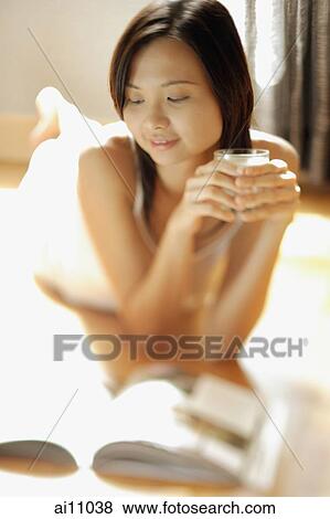 Stock Photo - Young woman lying on floor holding a glass, magazine open in front of her. Fotosearch