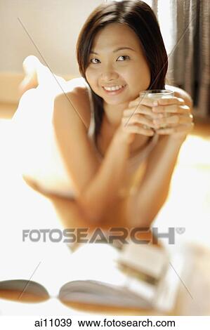 Young woman lying on floor holding a glass, looking at camera View Large Photo Image Stock Photo - Young woman lying on floor holding a glass, looking at camera. Fotosearch