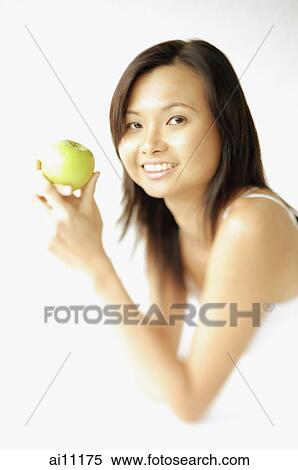 Stock Photography - Young woman lying on floor, holding apple, smiling at camera. Fotosearch