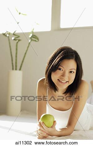 Young woman lying on front, holding green apple View Large Photo Image Stock Image - Young woman lying on front, holding green apple. Fotosearch