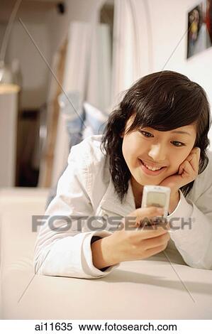 Young woman, lying on front, holding mobile phone View Large Photo Image Stock Photography - Young woman, lying on front, holding mobile phone. Fotosearch