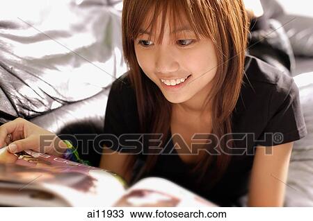 Young woman lying on sofa looking at magazine View Large Photo Image Stock Image - Young woman lying on sofa looking at magazine. Fotosearch