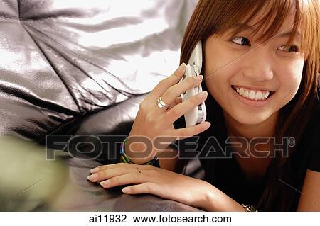 Stock Image - Young woman lying on sofa using mobile phone. Fotosearch