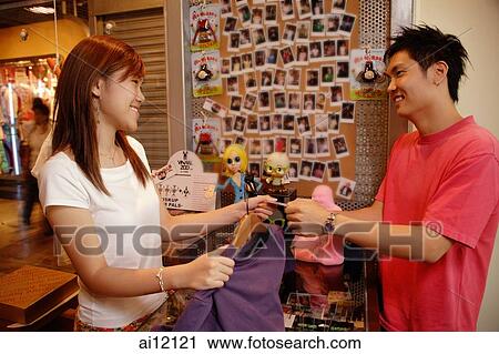 Stock Image -  Young woman making a purchase at a shop, passing store clerk a credit card. Fotosearch