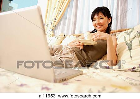 Young woman on bed with cup and saucer, looking at laptop View Large Photo Image Stock Image - Young woman on bed with cup and saucer, looking at laptop. Fotosearch