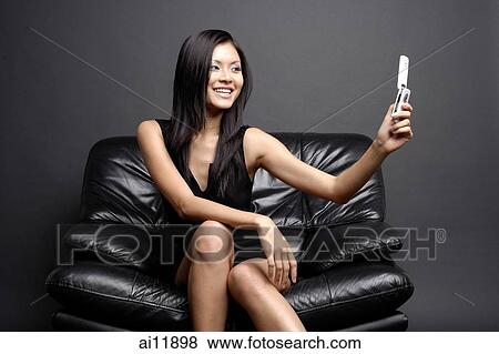 Young woman on black chair, looking at camera phone View Large Photo Image Stock Photo - Young woman on black chair, looking at camera phone. Fotosearch