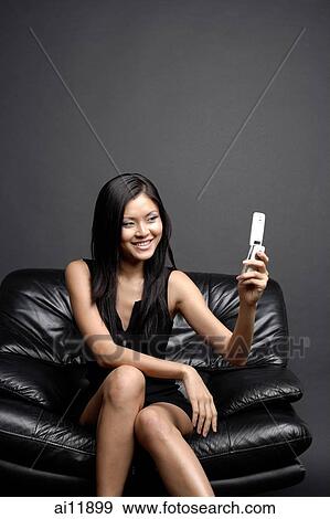 Young woman on black chair, looking at camera phone View Large Photo Image Stock Photo - Young woman on black chair, looking at camera phone. Fotosearch