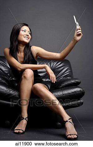 Young woman on chair holding camera phone View Large Photo Image Stock Image - Young woman on chair holding camera phone. Fotosearch