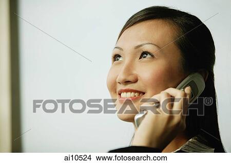 Picture - Young woman on mobile phone, looking up, smiling. Fotosearch
