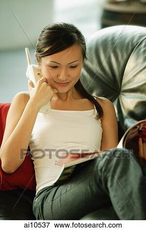 Young woman on sofa, holding phone and reading magazine View Large Photo Image Stock Photo - Young woman on sofa, holding phone and reading magazine. Fotosearch