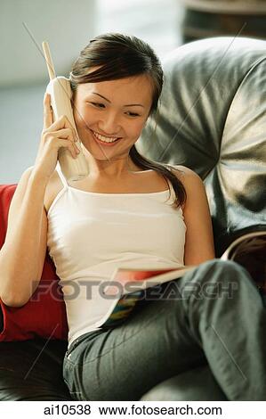 Young woman on sofa, holding phone and reading magazine View Large Photo Image Stock Photo - Young woman on sofa, holding phone and reading magazine. Fotosearch