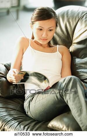 Young woman on sofa, looking at magazine View Large Photo Image Stock Image - Young woman on sofa, looking at magazine. Fotosearch