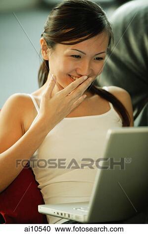 Young woman on sofa, using laptop, smiling View Large Photo Image Stock Image - Young woman on sofa, using laptop, smiling. Fotosearch