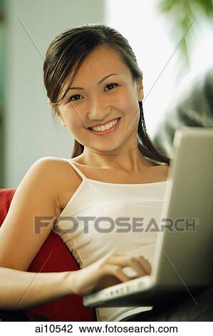 Young woman on sofa, using laptop, looking at camera View Large Photo Image Stock Image - Young woman on sofa, using laptop, looking at camera. Fotosearch