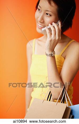Picture - Young woman on the phone, carrying shopping bags. Fotosearch