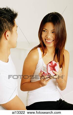 Young woman opening gift box, smiling at man next to her View Large Photo Image Stock Image - Young woman opening gift box, smiling at man next to her. Fotosearch
