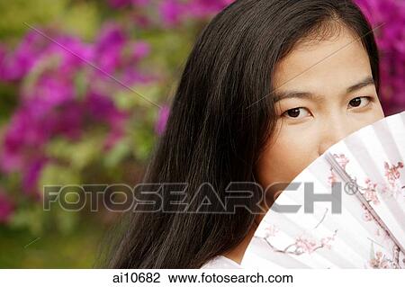 Stock Image - Young woman peeking over fan.. Fotosearch