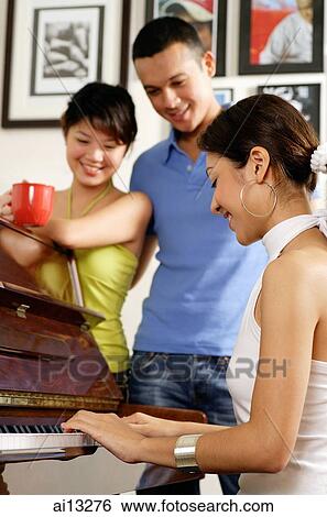 Young woman playing the piano, couple standing and watching her View Large Photo Image Stock Photograph - Young woman playing the piano, couple standing and watching her. Fotosearch