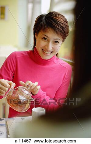 Stock Photo - Young woman pouring tea, facing another woman. Fotosearch