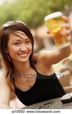 Young woman raising a glass of beer, looking at camera View Large Photo Image Stock Image - Young woman raising a glass of beer, looking at camera. Fotosearch