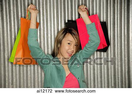 Stock Image -  Young woman raising shopping bags over shoulder, smiling. Fotosearch