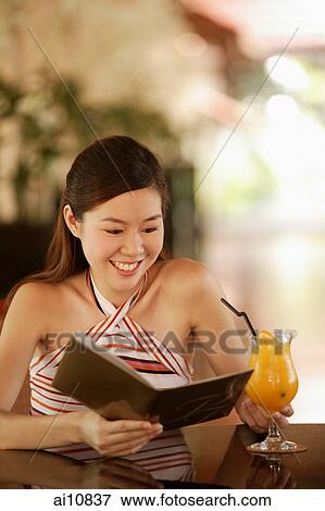 Stock Photo - Young woman reading menu, drink on the table in front of her. Fotosearch
